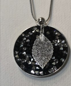 Pendentif réalisé avec des strass de Swarovski sur un support médaillon argenté , accompagné d'une petite breloque argentée en forme de feuille ajouré .